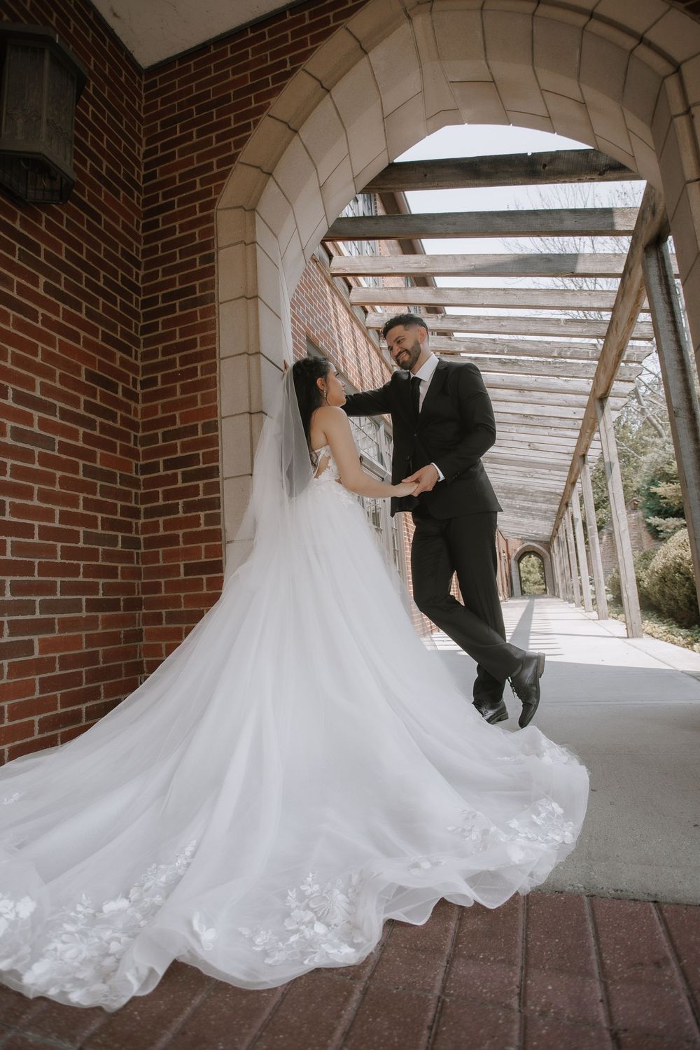 A couple dances playfully under a covered brick walkway, with the bride's white gown swirling around them.