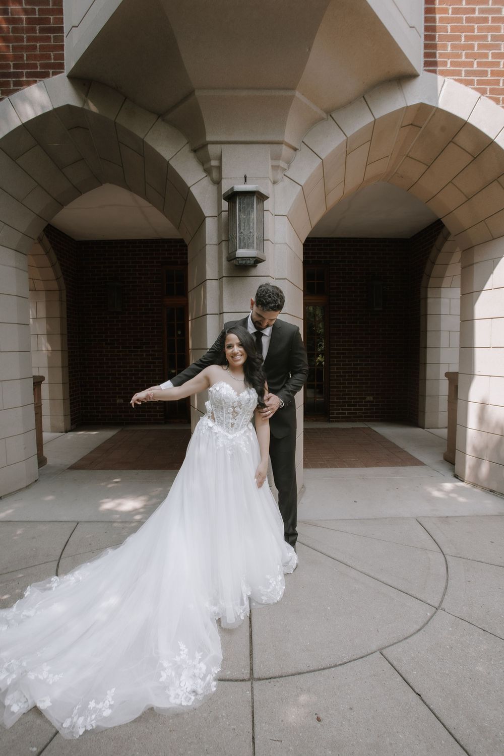 A romantic bridal portrait series under arched brick walkways showing the flowing train of a lace wedding dress.