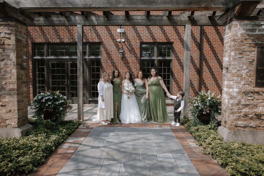 Wedding party group arranged near stone columns and greenery of a historic building exterior.
