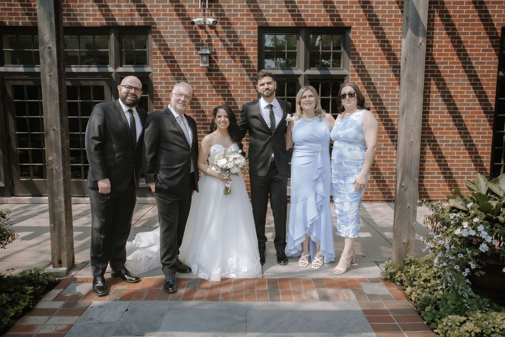A wedding party poses together in front of a brick building with exposed timber beams.