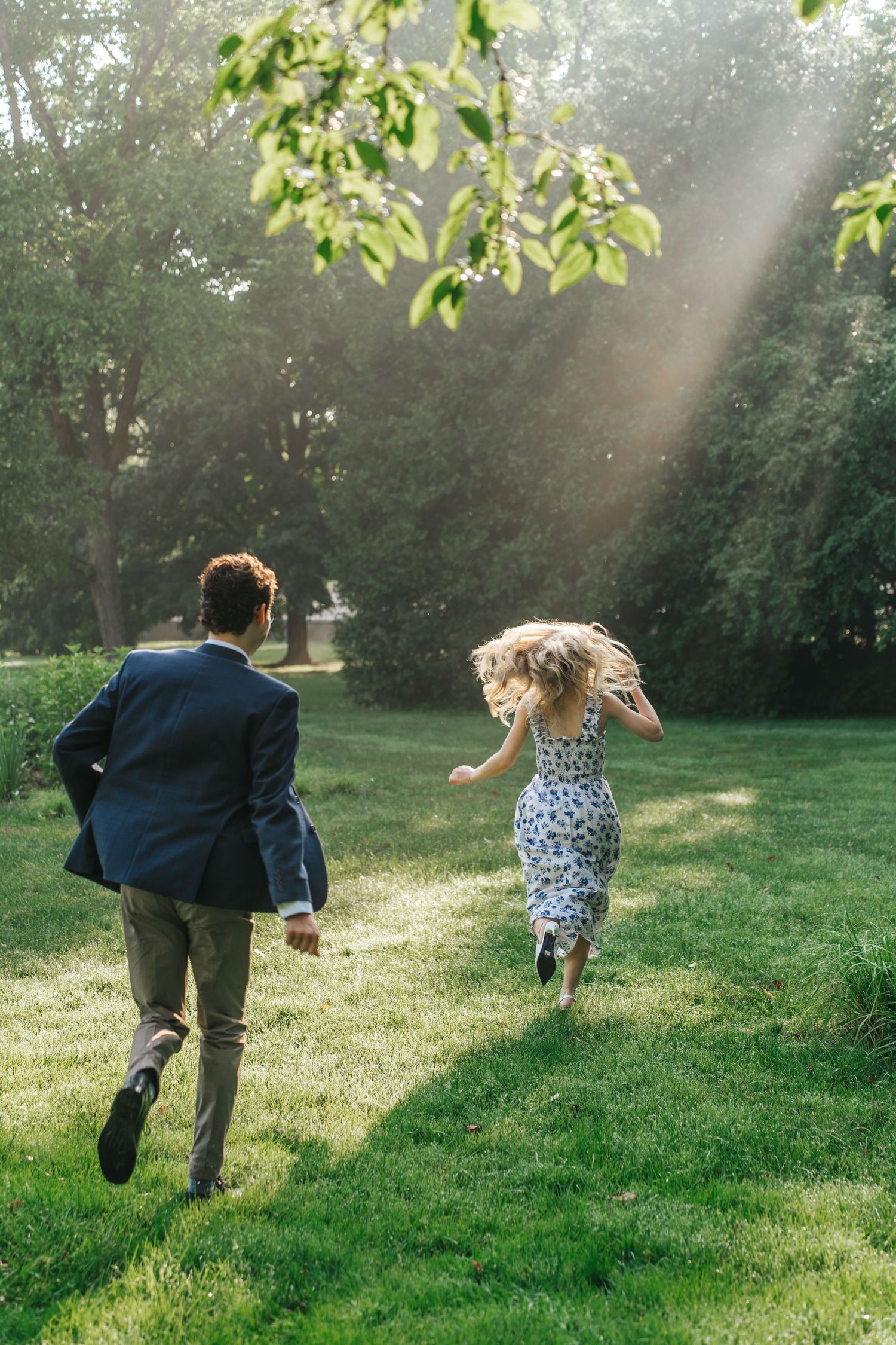 Couple running playfully through a sunlit garden with streaming rays overhead.