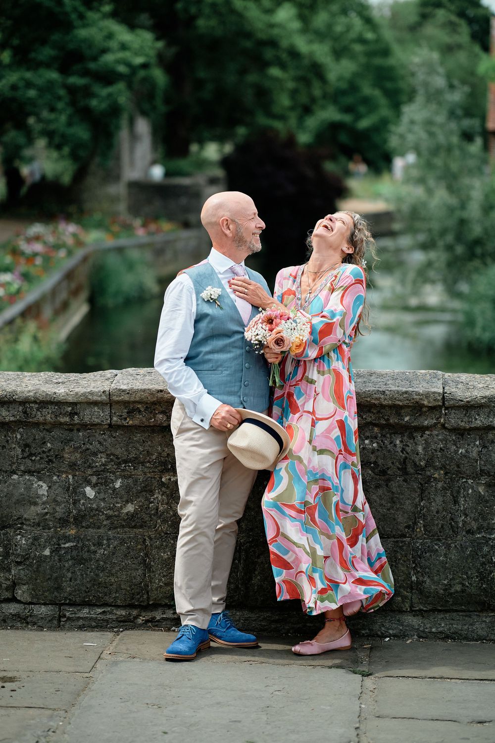 A couple shares a romantic moment on stone steps surrounded by lush greenery, with her in a colorful dress and him in a vest.