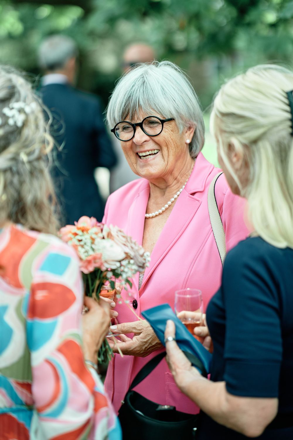 A group of people engaged in lively conversation at an outdoor social gathering, with someone wearing a bright pink blazer.