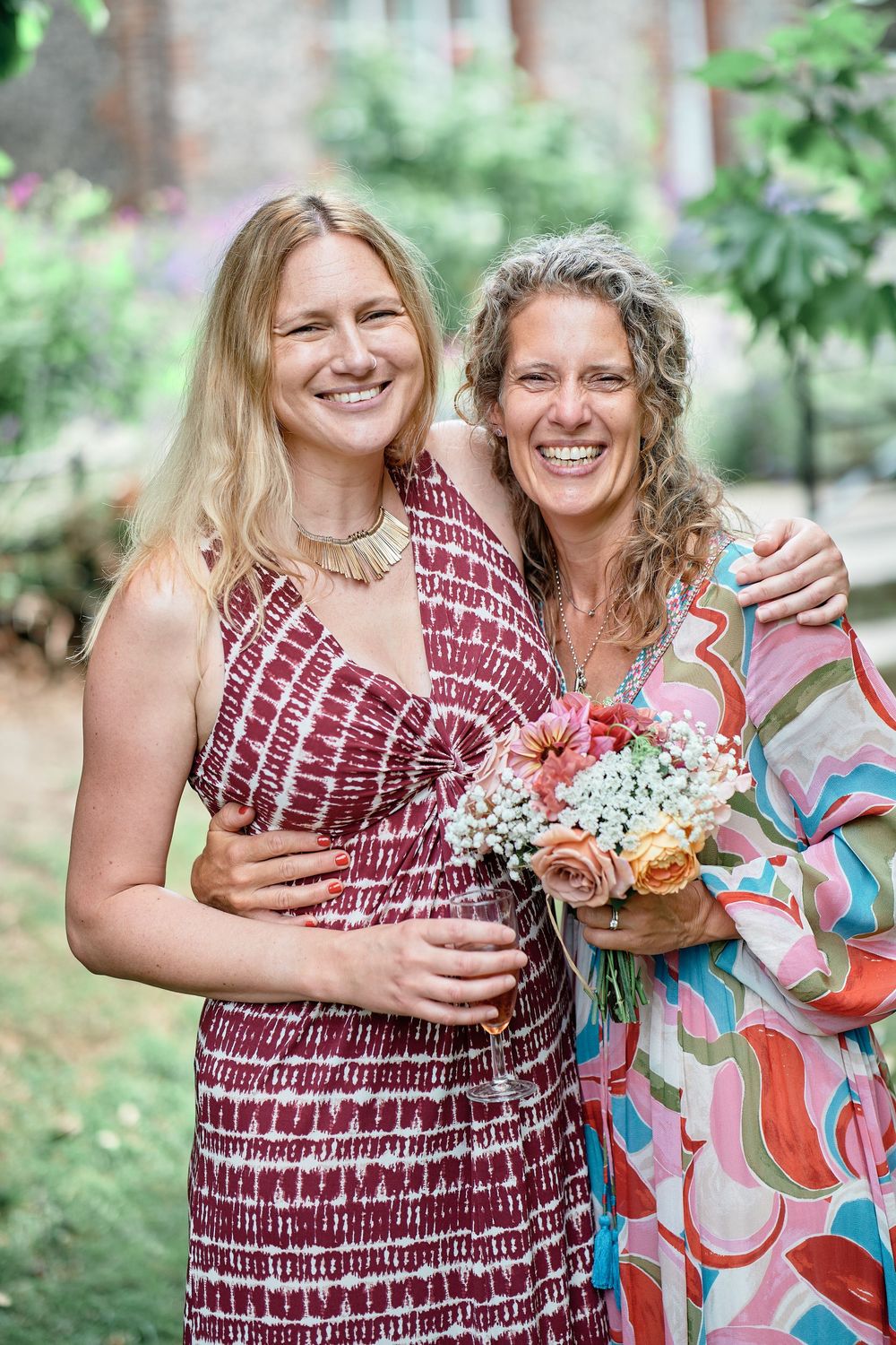 Two people in coordinating summer dresses share happy moments in a lush garden setting.