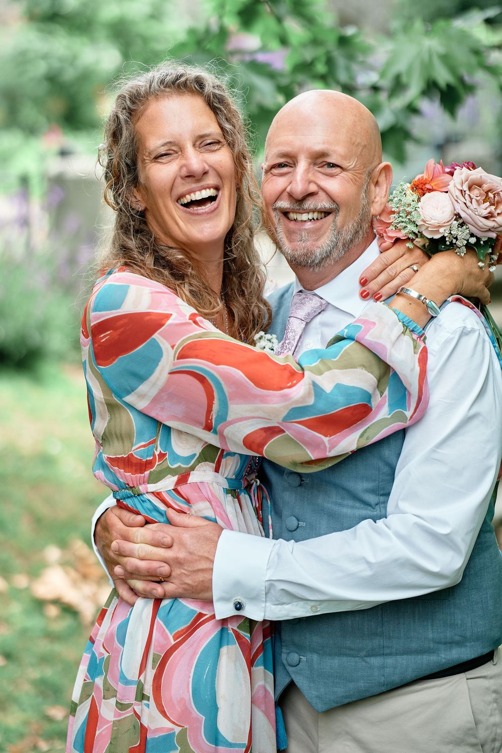 A couple shares joyful embraces and laughter in an outdoor garden setting wearing casual attire and colorful clothing.