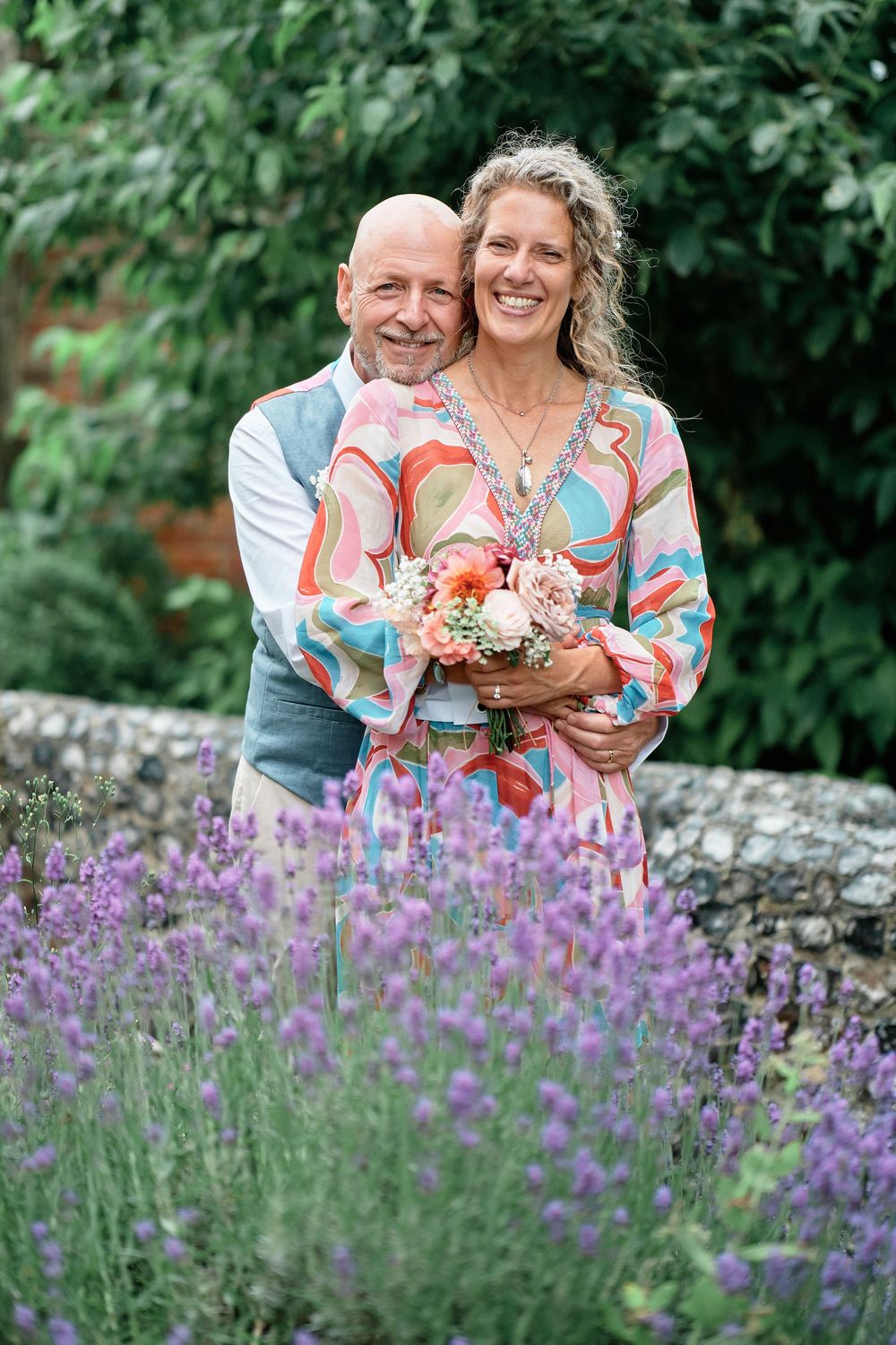 A couple embraces in a garden with blooming purple lavender flowers in the foreground.