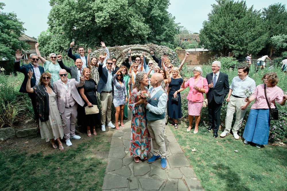 Wedding guests toss colorful flower petals and confetti at celebrating couple in outdoor garden celebration.