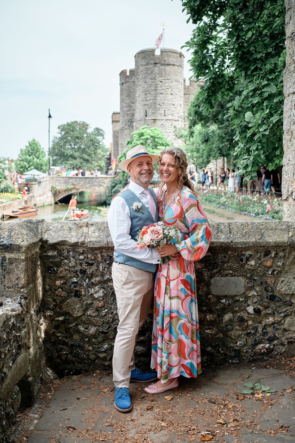 A couple stands together at a historic stone castle wall during a summer photoshoot enjoying a playful moment.