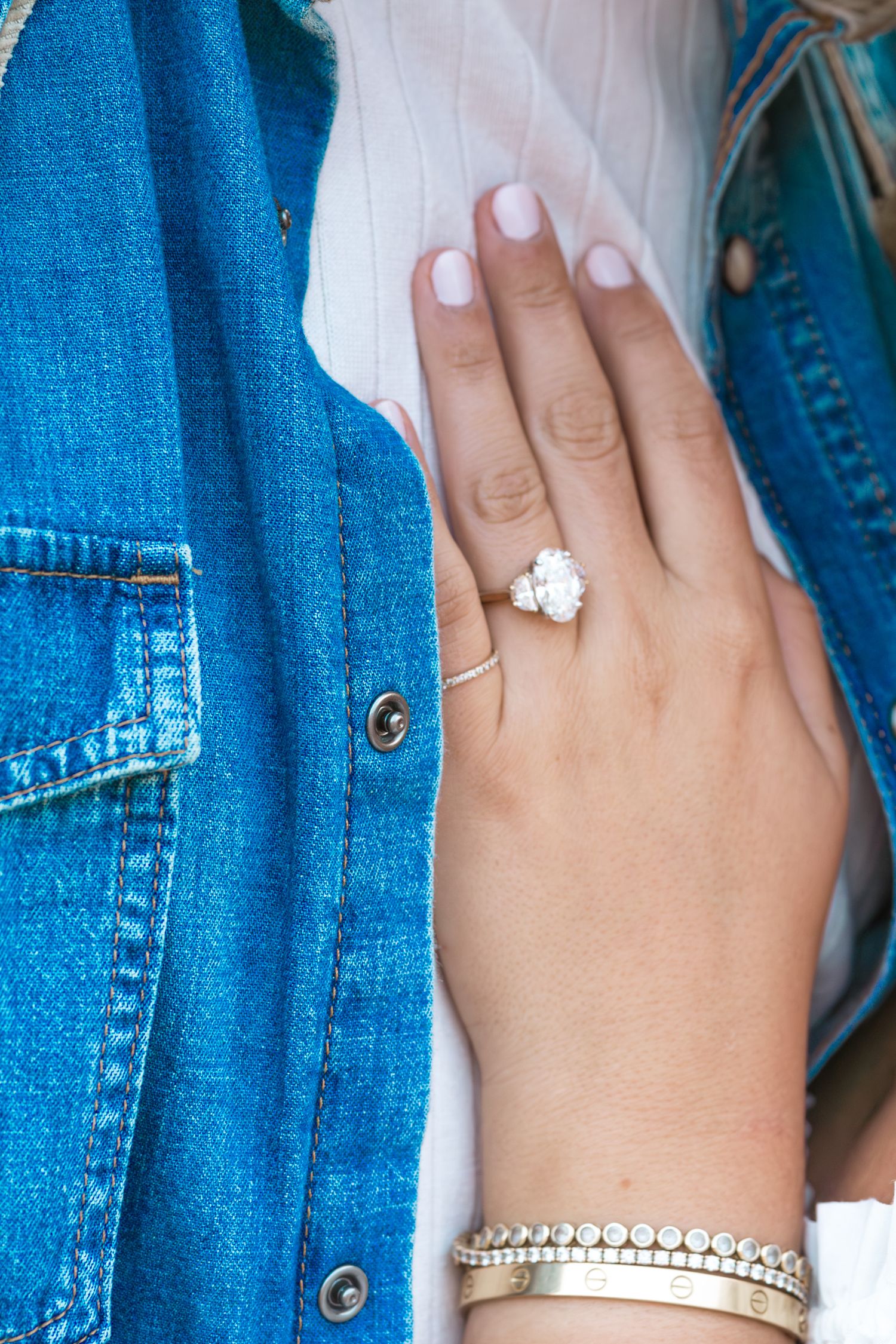 Close-up view of hands wearing white nail polish and jewelry against denim blue fabric background. Engagement ring Knoxville.