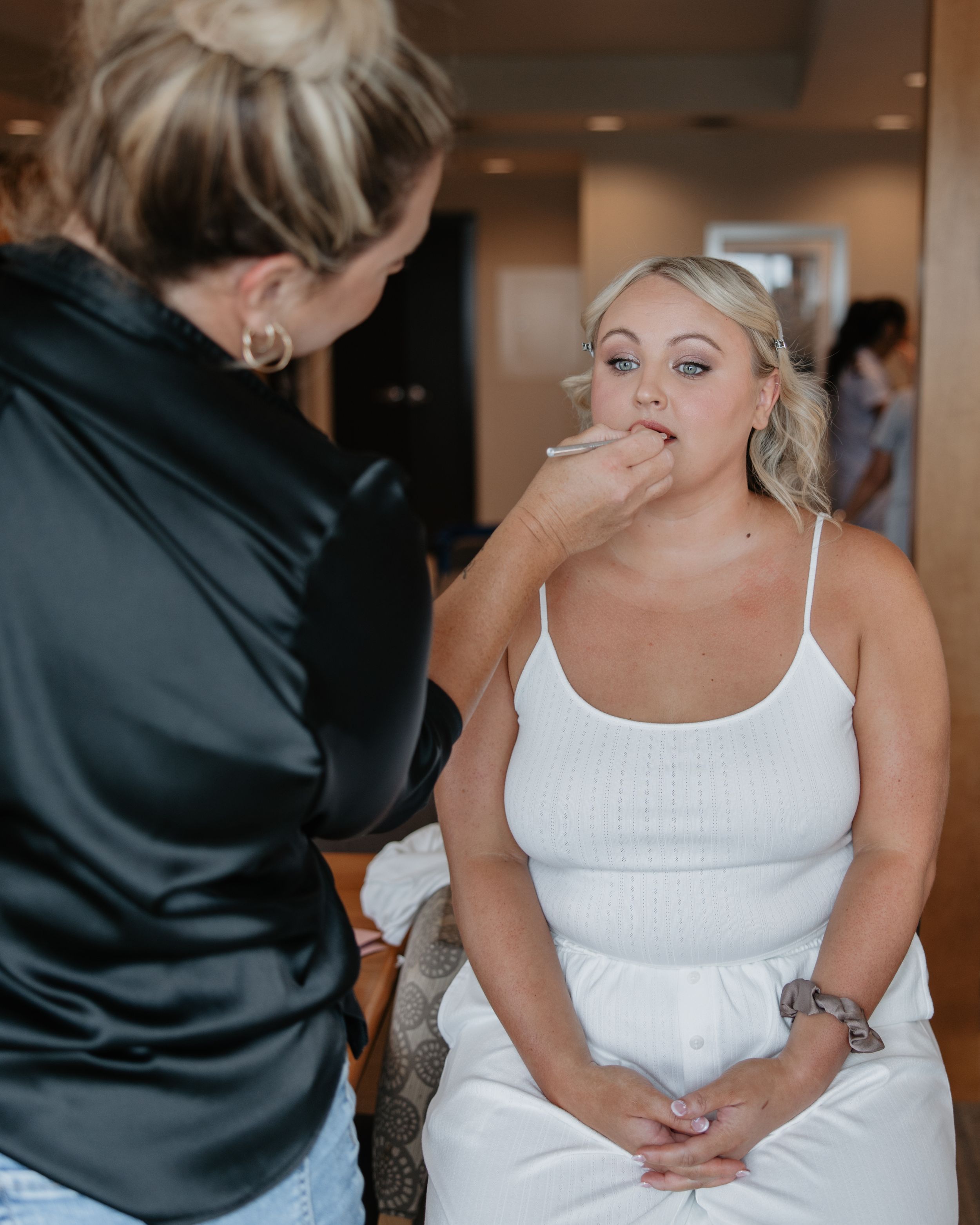 A makeup artist applies cosmetics to a person wearing a white dress during wedding preparation.