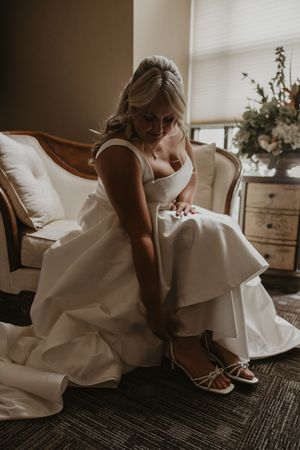 Close-up sequence shows a white wedding dress and shoes being put on against a carpeted floor in warm lighting.