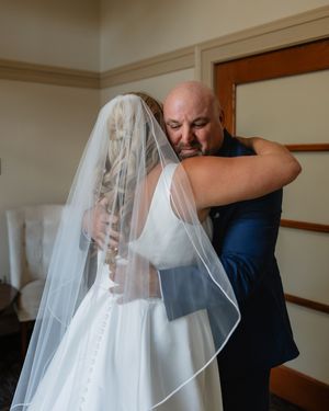 A romantic moment between a bride in white dress and someone wearing a navy suit during a wedding ceremony.