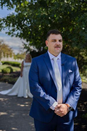 A groom in a navy blue suit and white tie standing outdoors during a first look wedding moment.