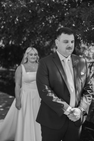 A wedding party group enjoys candid moments outdoors under trees in black and white photography.