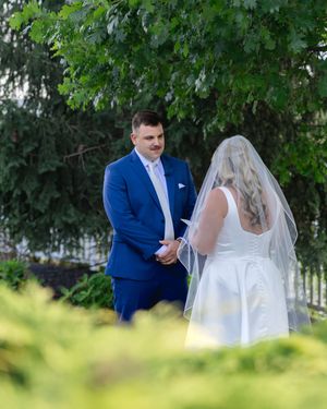 A romantic first look sequence between newlyweds surrounded by lush green trees in an outdoor garden setting.