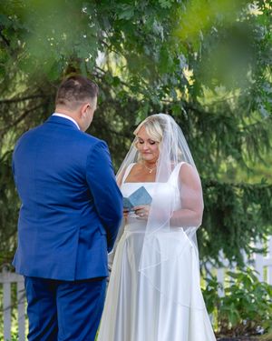 A couple shares an intimate outdoor wedding ceremony moment surrounded by lush greenery.
