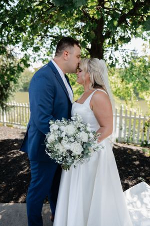 Wedding couple shares intimate moments in a garden setting with white floral bouquet and navy suit.
