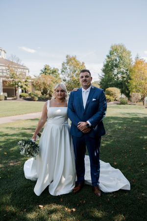 Wedding couple poses together on a sunny autumn day on grassy hill in formal attire.