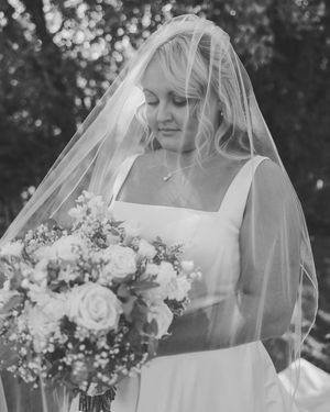 A black and white portrait of a bride wearing a veil and holding a bouquet of roses with a soft, dreamy expression.