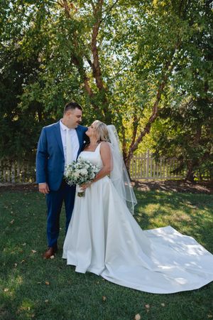 Elegant outdoor wedding photos captured in a garden with flowing white dress and blue suit.