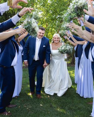 Wedding party in navy and white attire celebrating joyfully on green lawn.