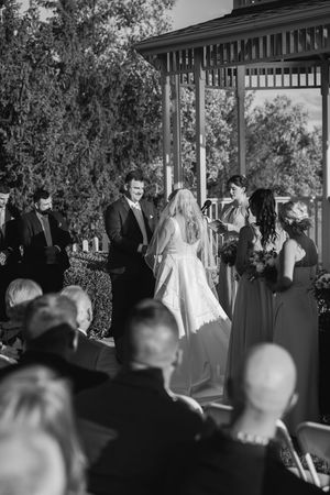 Black and white silhouettes of wedding guests watching a ceremony from behind in an outdoor venue.