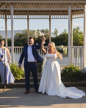 Wedding party poses under elegant white gazebo surrounded by lush greenery during sunset celebration.