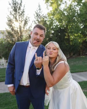 A playful moment captured between a bride in white and groom in navy blue making silly faces at their wedding.