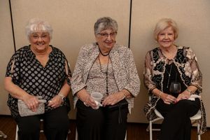 A group portrait of elderly women dressed in black and white outfits sitting together in a row.