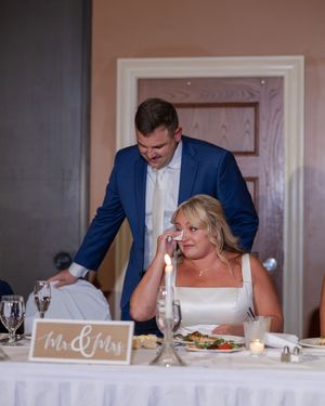 A couple shares an emotional moment at their wedding reception table with a 'Mr & Mrs' sign visible.