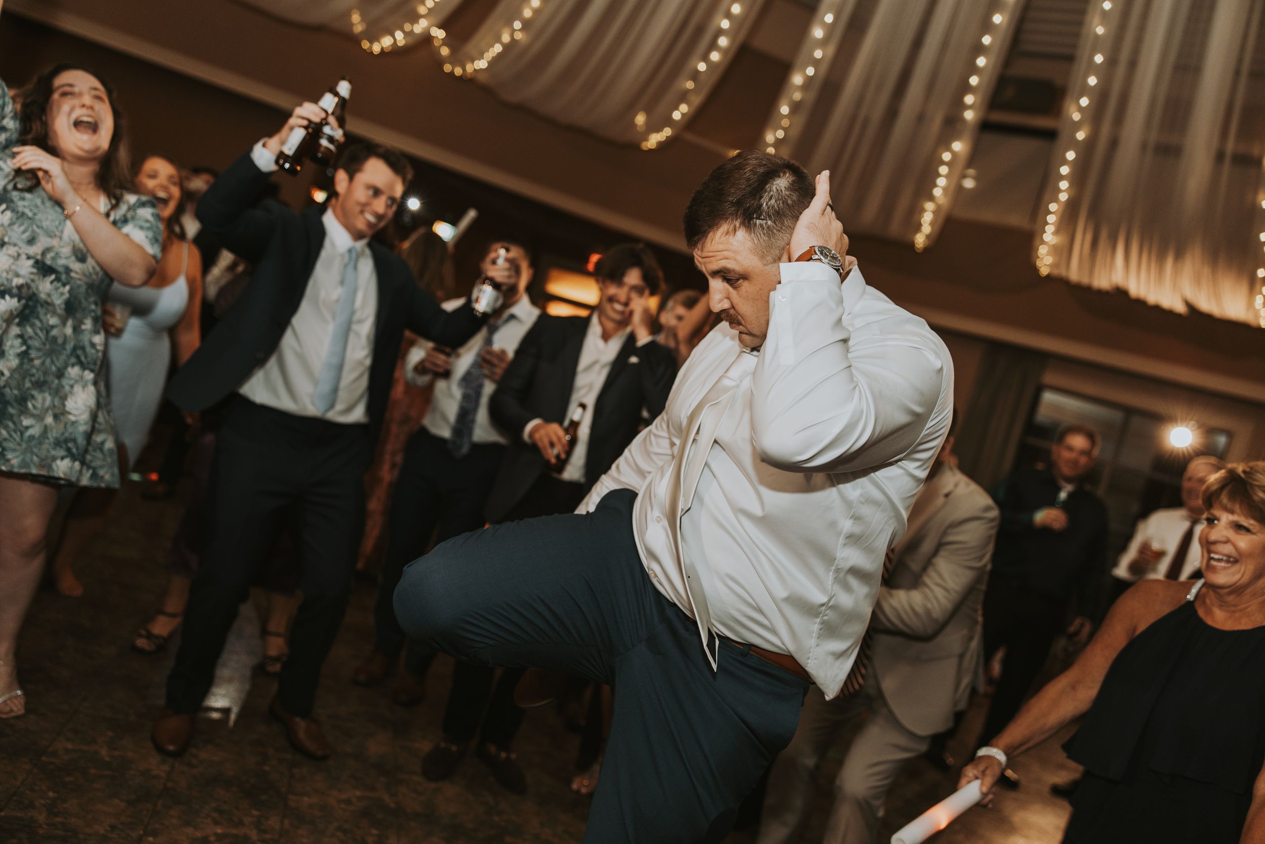 Wedding reception guests enjoying dancing together on a dimly lit dance floor under decorative string lights.