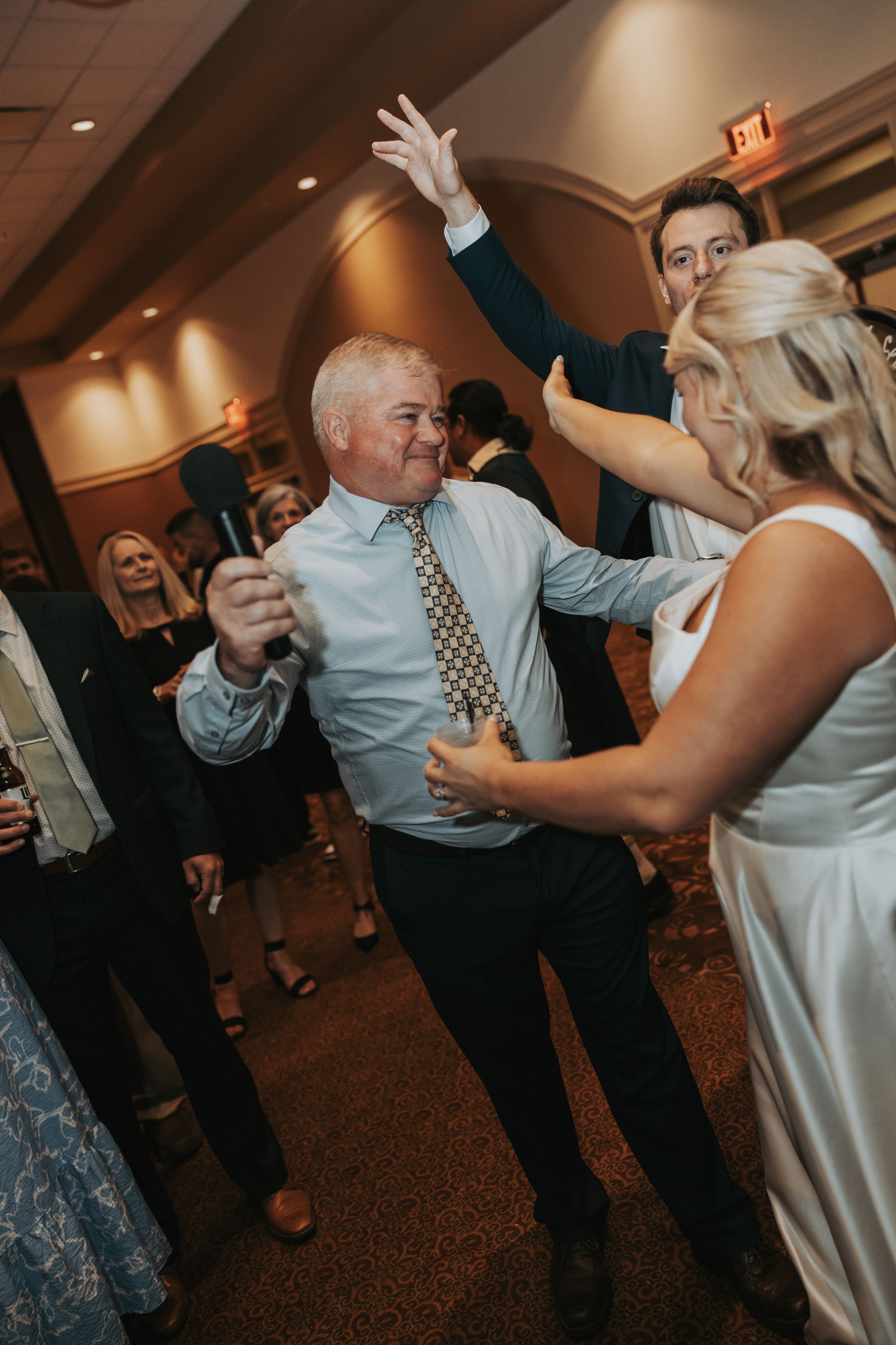People dancing together at a wedding reception in a warmly lit indoor venue.