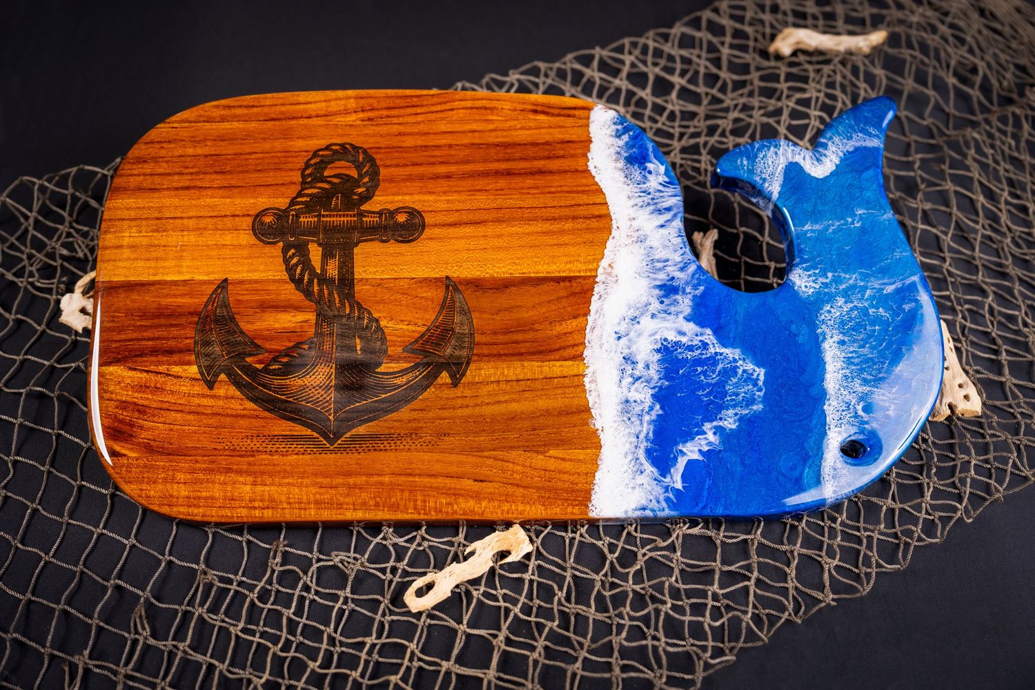 Wooden serving board with anchor design and blue ocean resin inlay surrounded by fishing net.