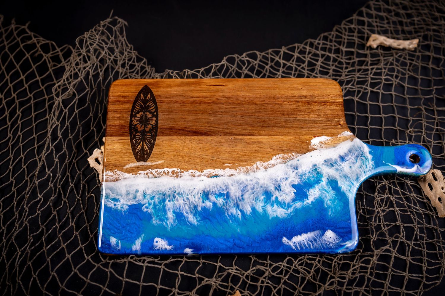 Ocean wave resin art on wooden serving board with blue epoxy creating realistic water effect against fishing net backdrop.