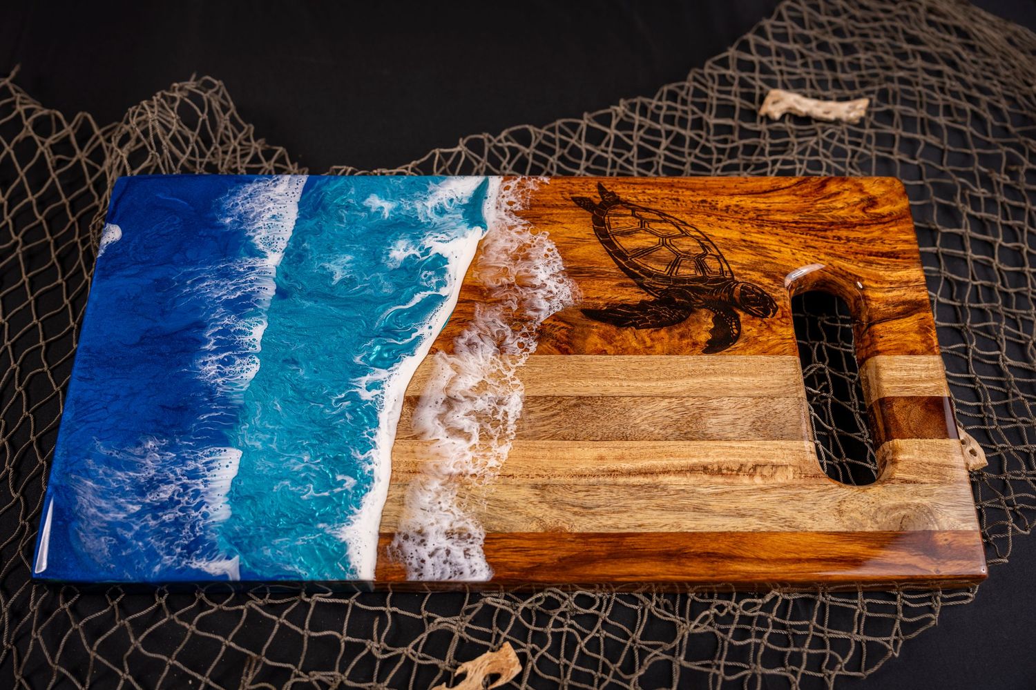 Handcrafted wooden cutting board featuring ocean waves in blue resin creating a beach scene on dark net background.