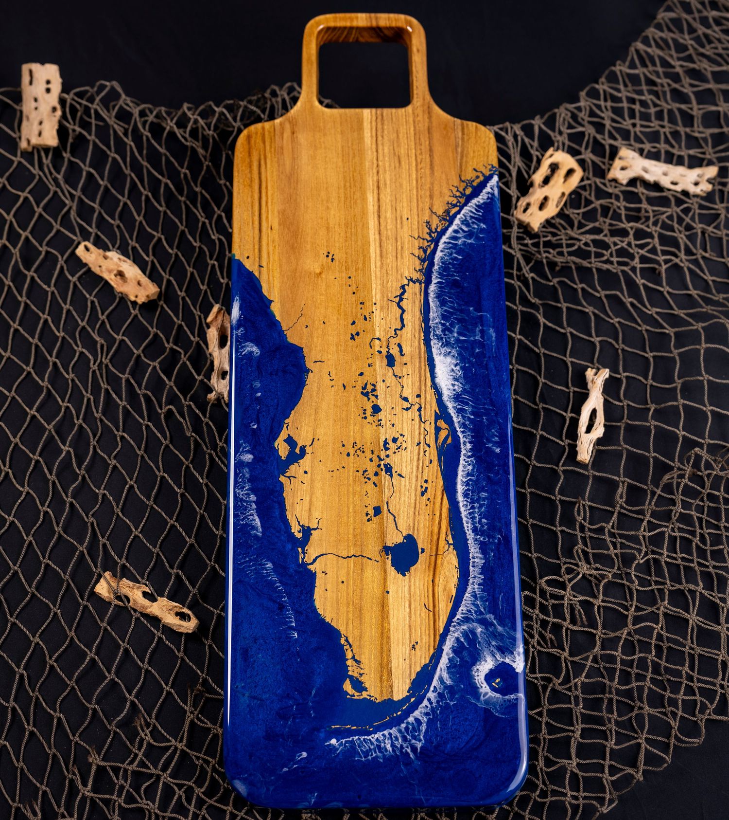 Wooden serving board with blue epoxy resin ocean design and fishing net backdrop.