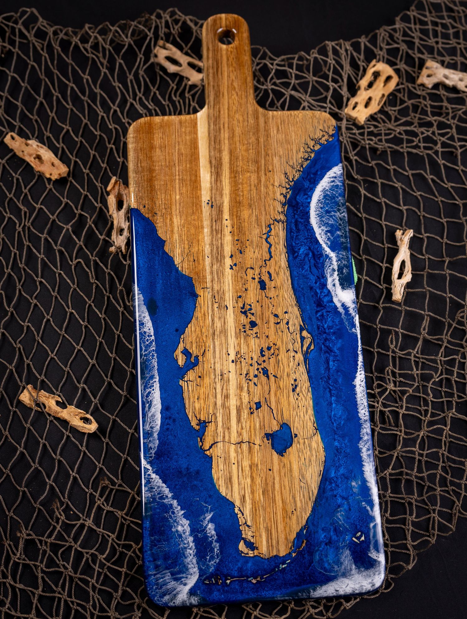 Coastal-inspired resin artwork on wooden board displays flowing blue patterns with decorative fishing net background.