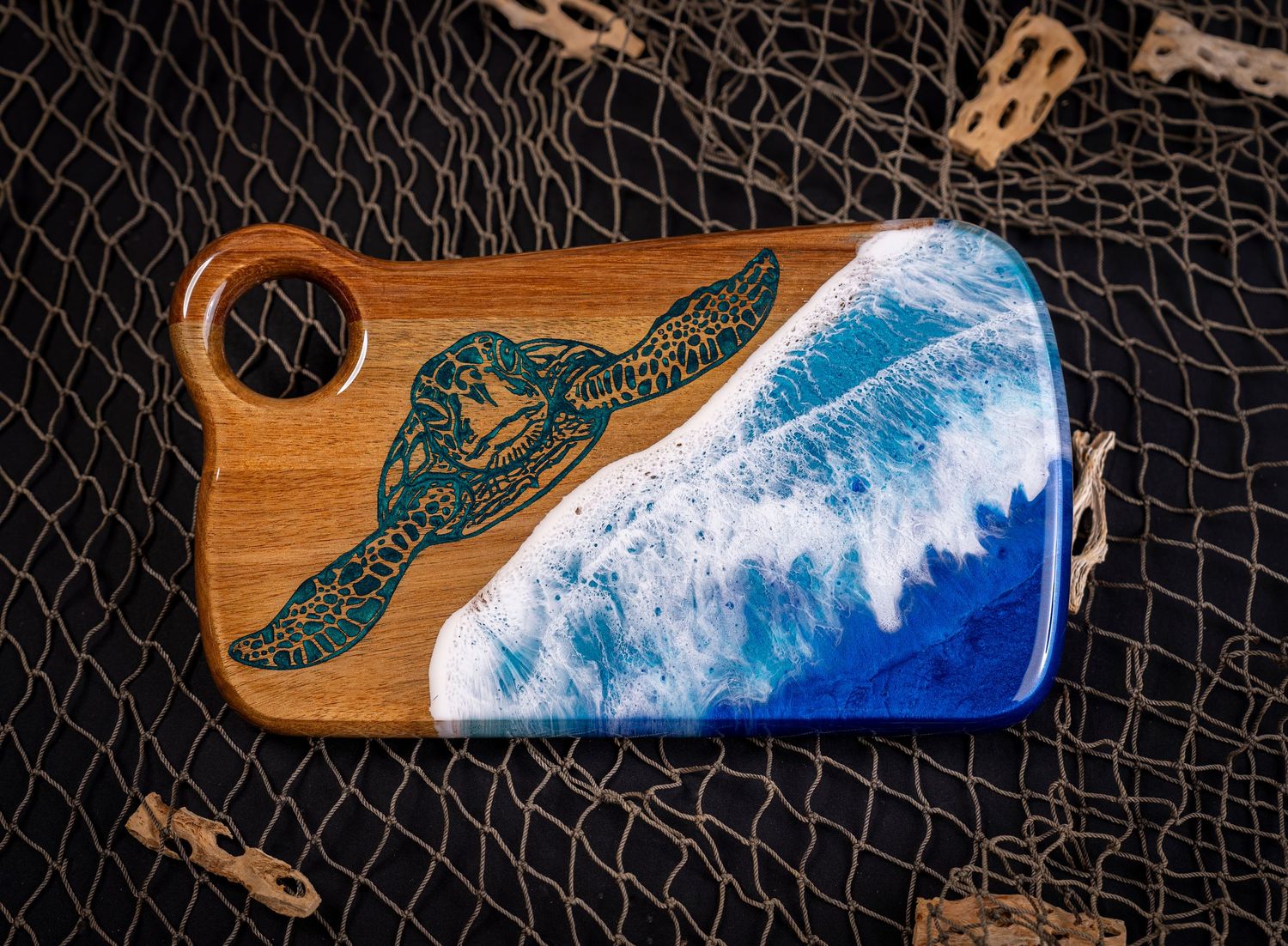 Handcrafted wooden serving board featuring a sea turtle design and ocean wave resin art against a fishing net background.