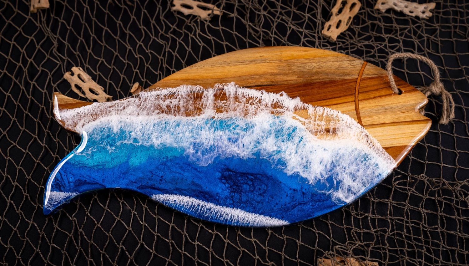 Fish-shaped wooden serving board decorated with blue ocean wave resin art displayed on fishing net.