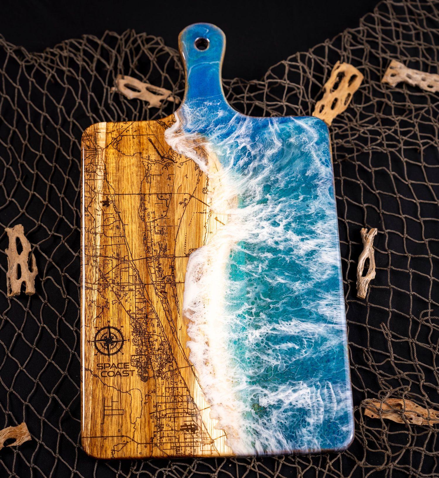 Creative resin art design combining wooden cutting board and blue epoxy resembling ocean waves inside a fishnet backdrop.