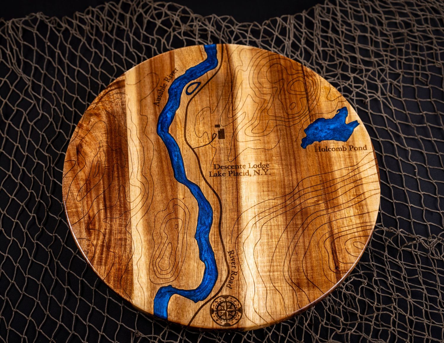 A round wooden charcuterie board featuring blue epoxy resin river inlay design on natural wood grain surface.