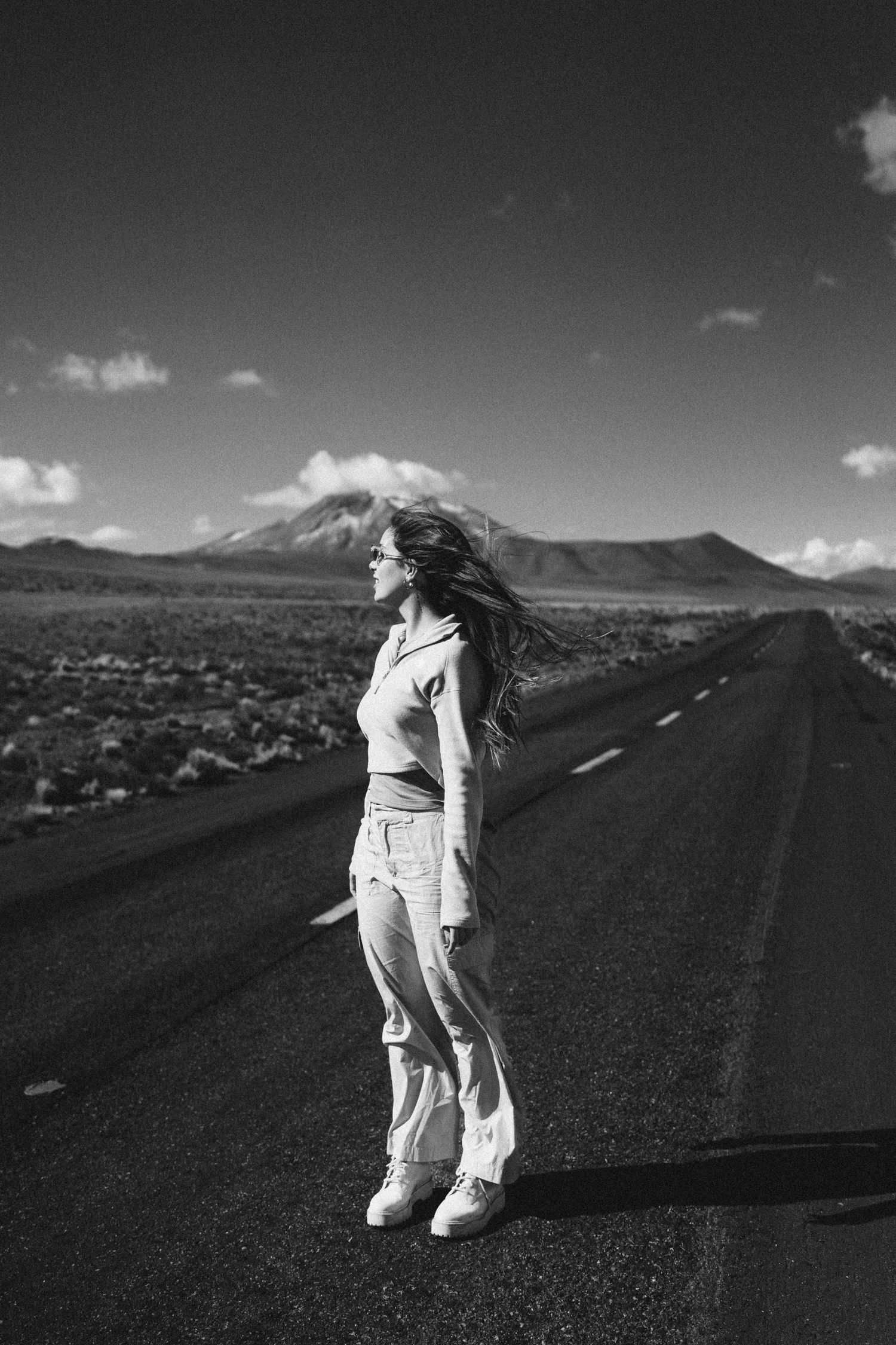 Lone figure stands on empty mountain road against dramatic landscape backdrop.