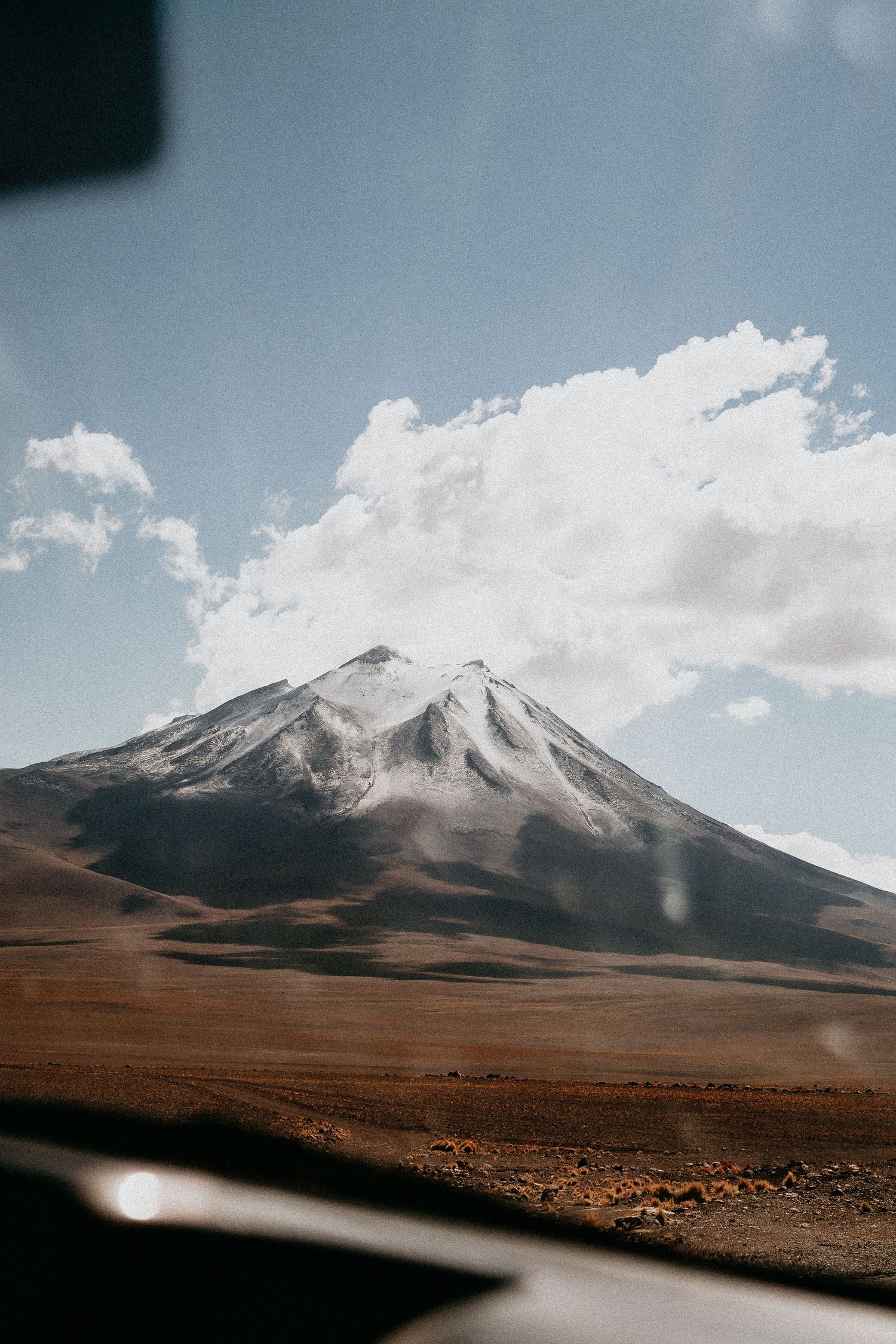 Majestic snow-capped volcano peak rises above desert plains under blue sky.