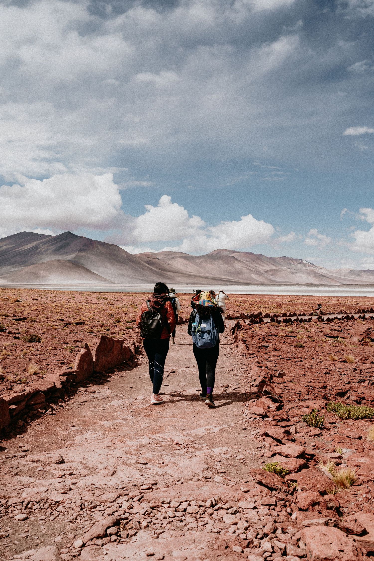Two adventurers hiking along desert trail with mountains in the distance.