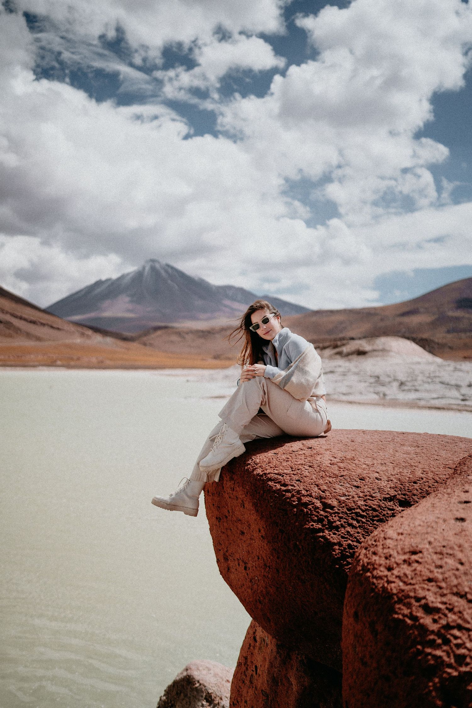 Person lounging on red rocks against a stark desert landscape with mountains and white clouds in the background.