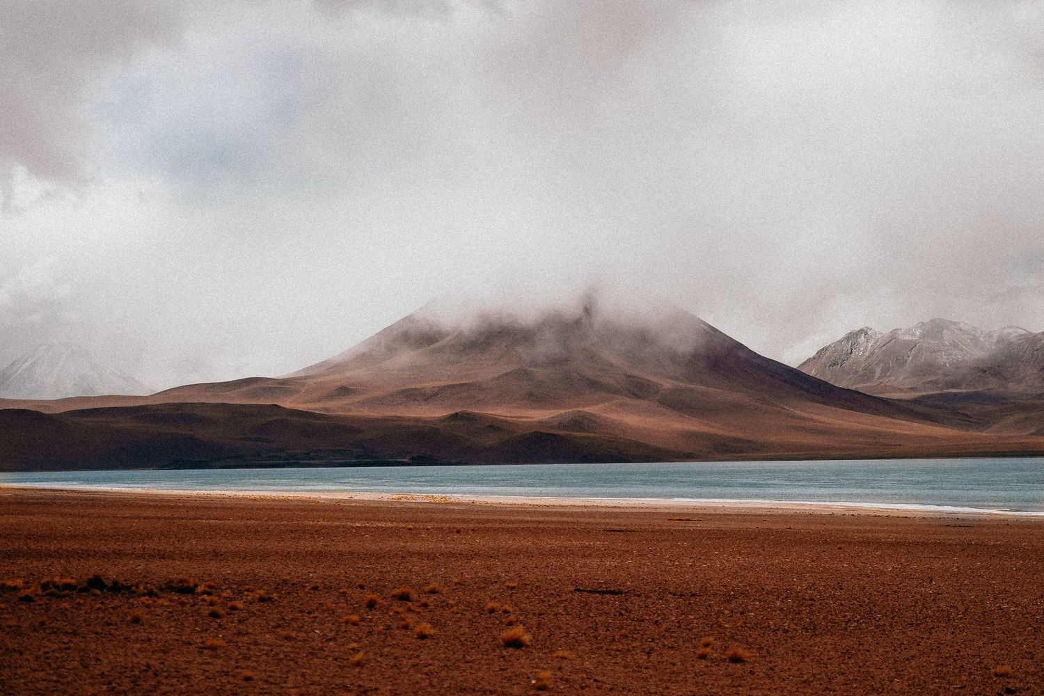 Panoramic view of desert terrain with mountains and lake under cloudy skies.