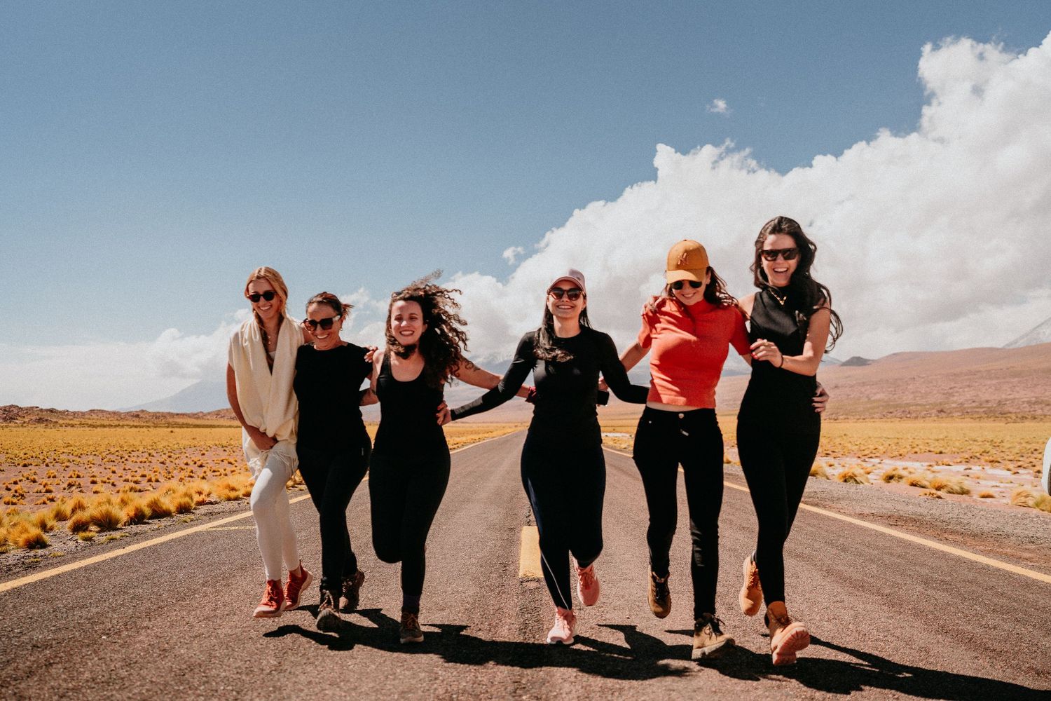 Group walking and posing together on desert road with mountains in background.