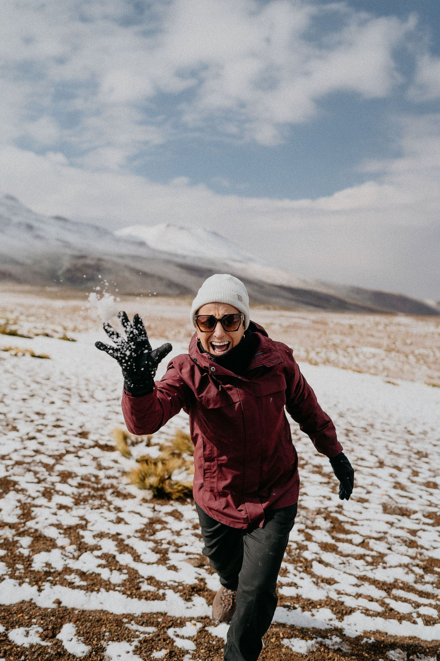 Adventurer in a burgundy jacket and white beanie enjoying a snowy mountain landscape.