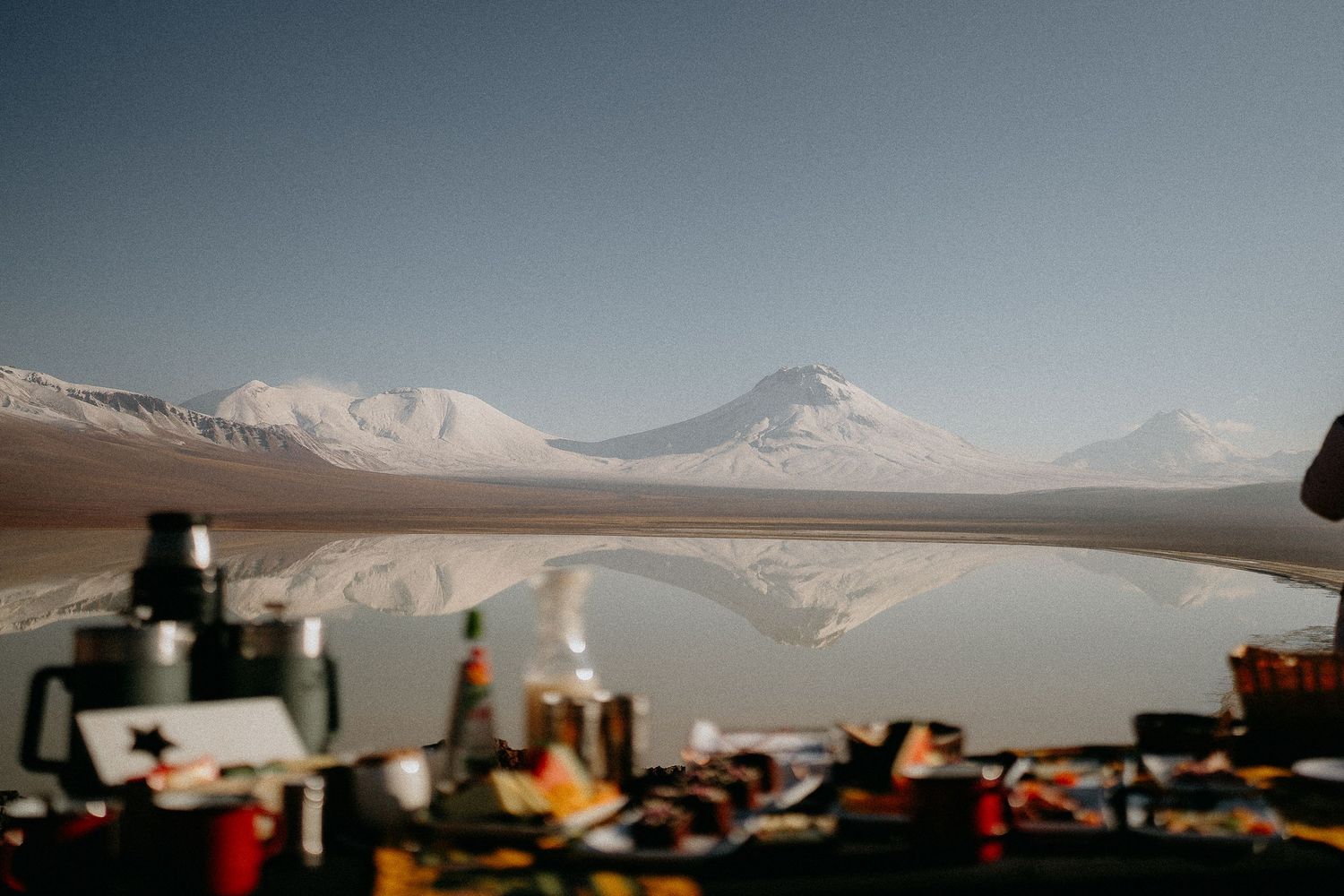 Camping gear and equipment laid out with snow-capped mountains and a reflective lake in the background.