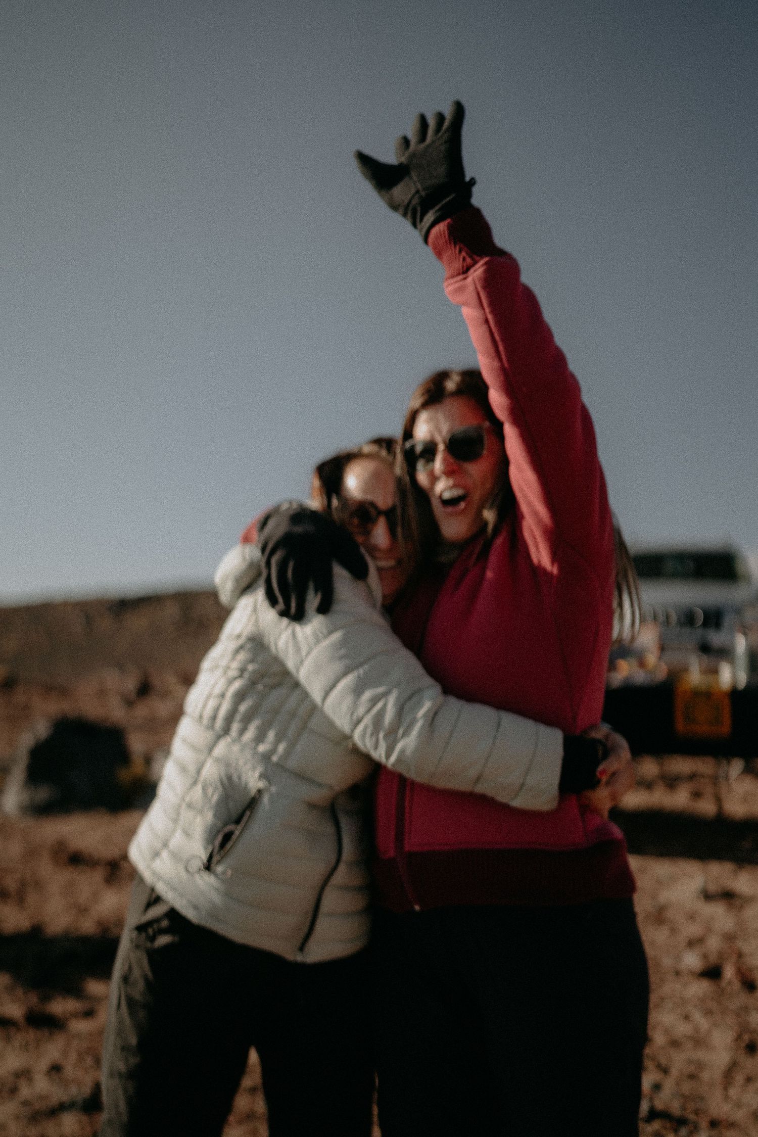 Friends celebrating and hugging outdoors in winter jackets against a desert landscape.